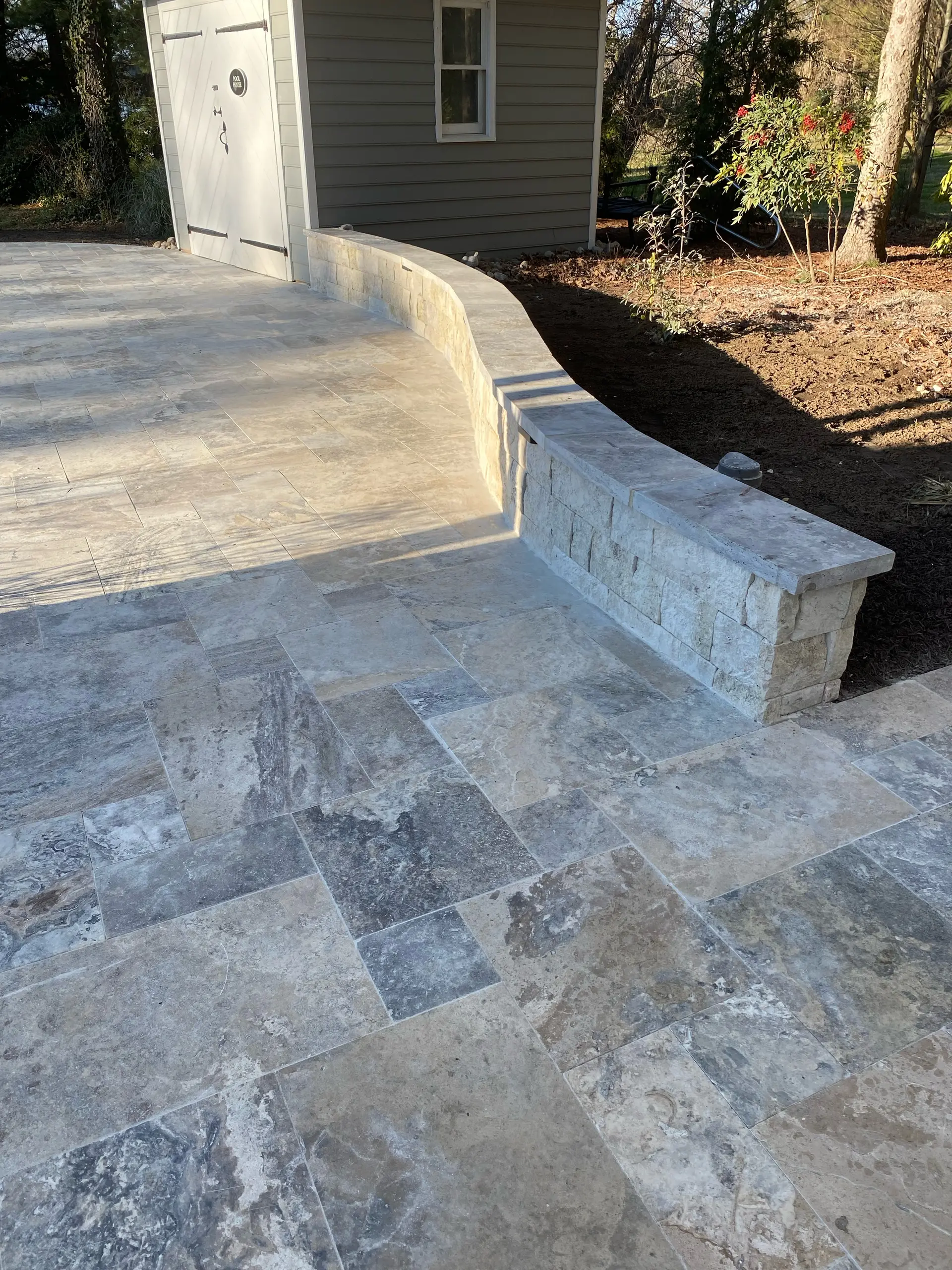 Stacked-stone retaining wall integrated with a travertine paver patio